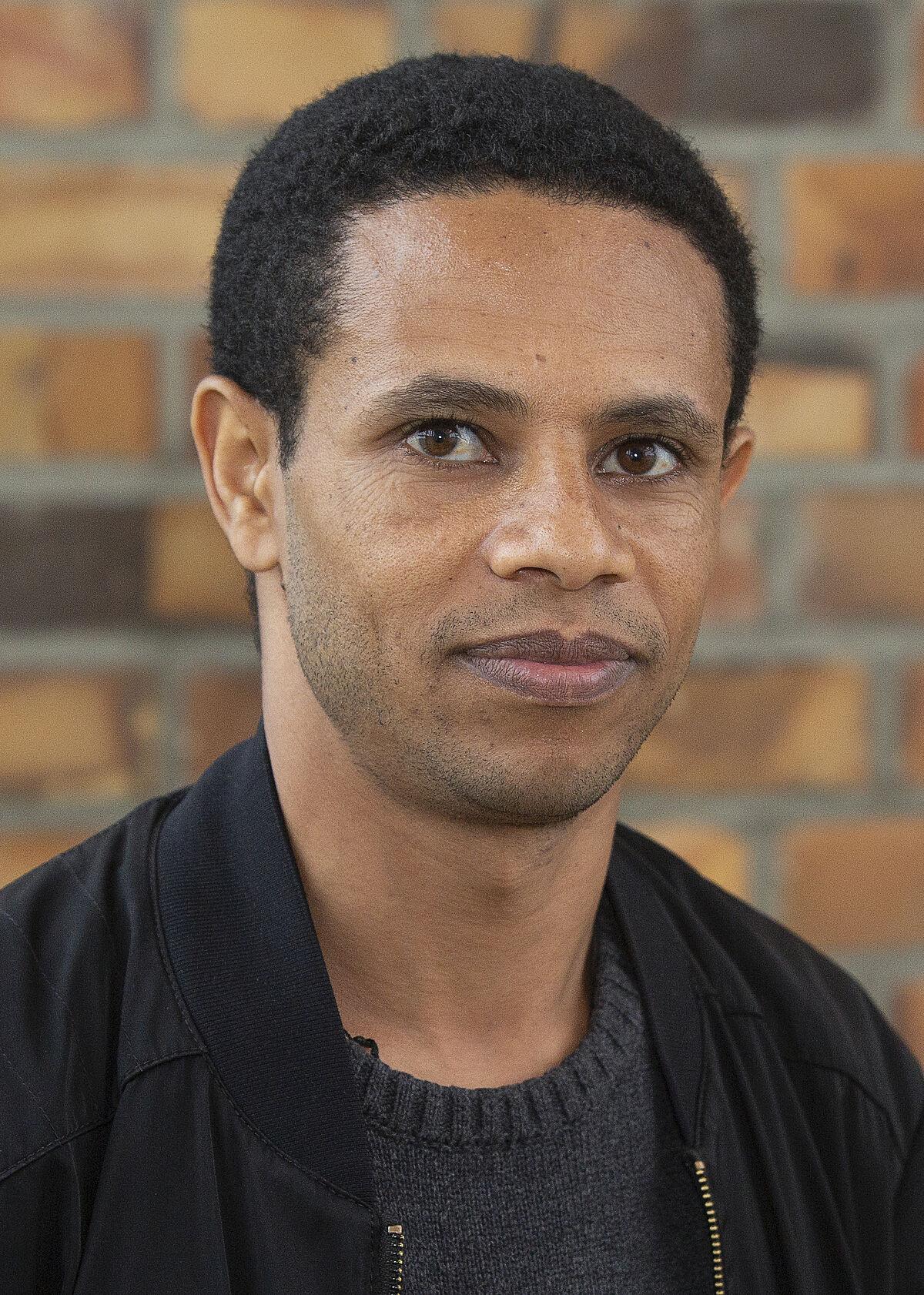 Portrait Sintayehu Legesse in front of a stone wall